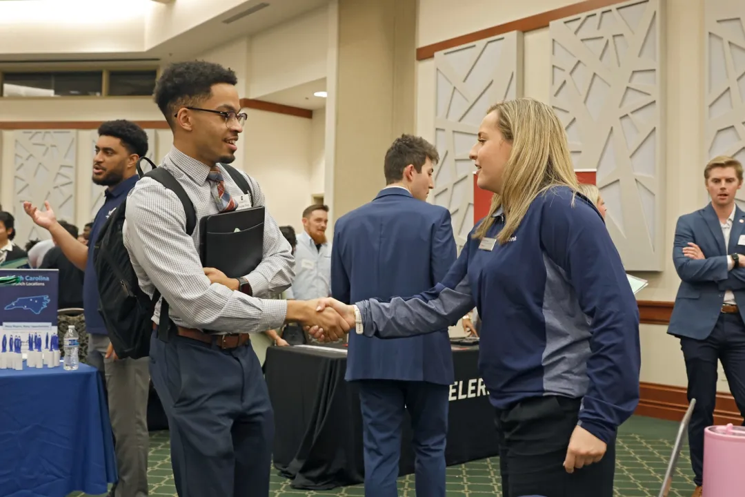 A student shaking hands with an employee at the Belk Career Fair